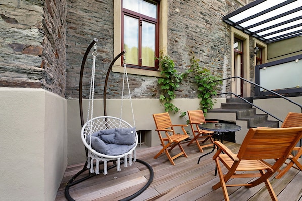 A wooden deck with a hanging chair, wooden chairs, and a table.