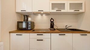 Een compacte keuken met witte kastjes, een magnetron, een koffiezetapparaat en een spoelbak.