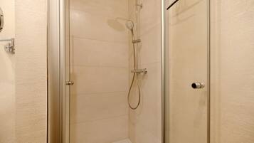 Una ducha con cerramiento de vidrio, un cabezal de ducha de mano y un grifo de pared.