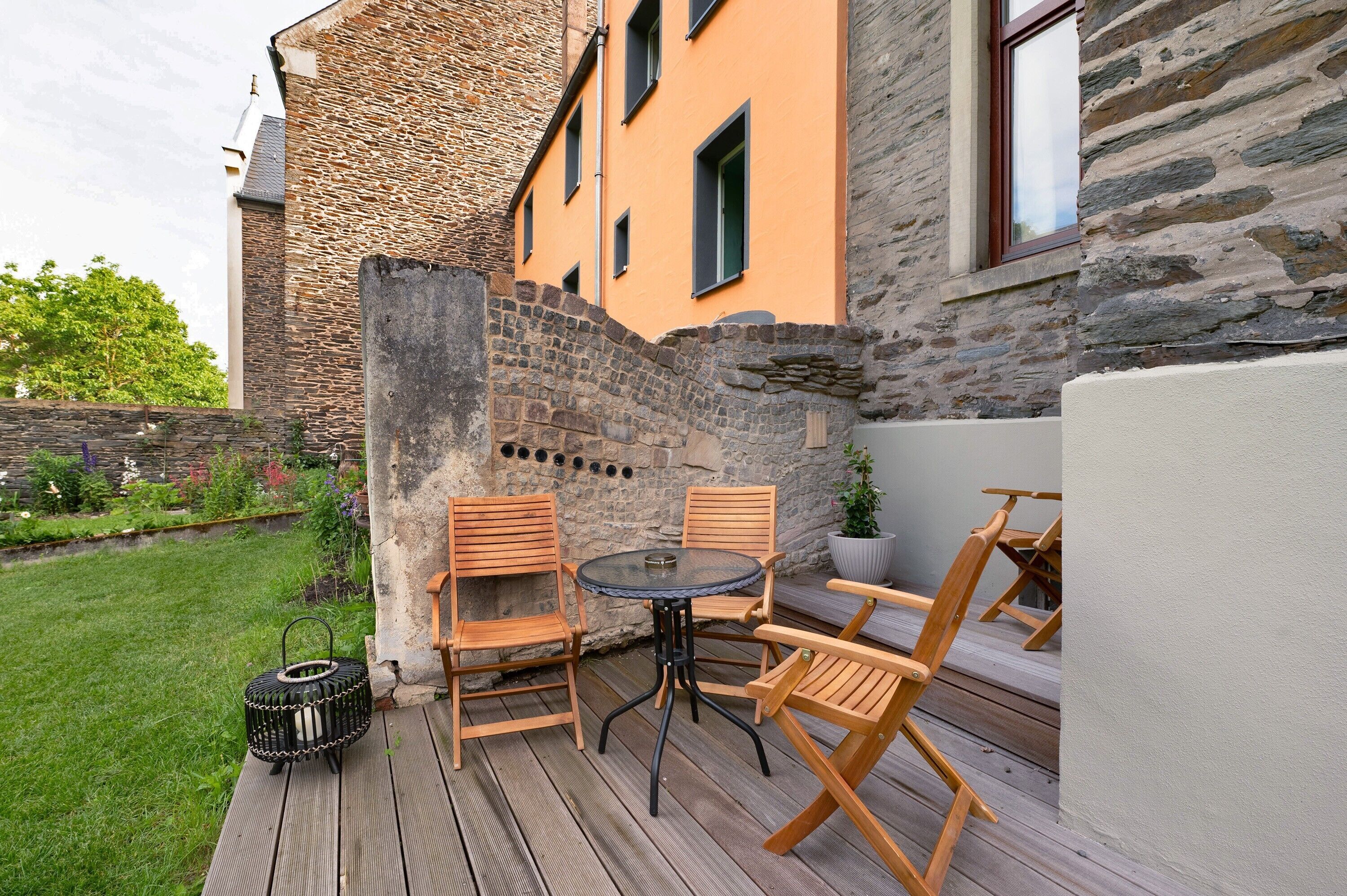 A patio with a round table and four wooden chairs, a small black basket, and a potted plant.