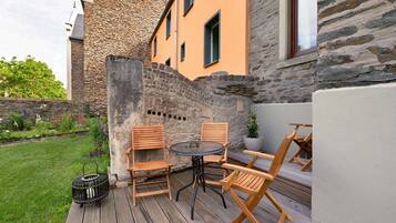 A patio with a round table and four wooden chairs, a small black basket, and a potted plant.