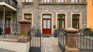 Un bâtiment en pierre avec une porte rouge, un balcon et une entrée fermée par un portail.