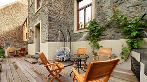 Une terrasse en bois avec des meubles d’extérieur, un fauteuil suspendu et un bâtiment en pierre doté d’une fenêtre.