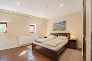 Un dormitorio con una cama de madera, dos mesitas de noche con lámparas, un radiador y una ventana con vistas a zonas verdes.