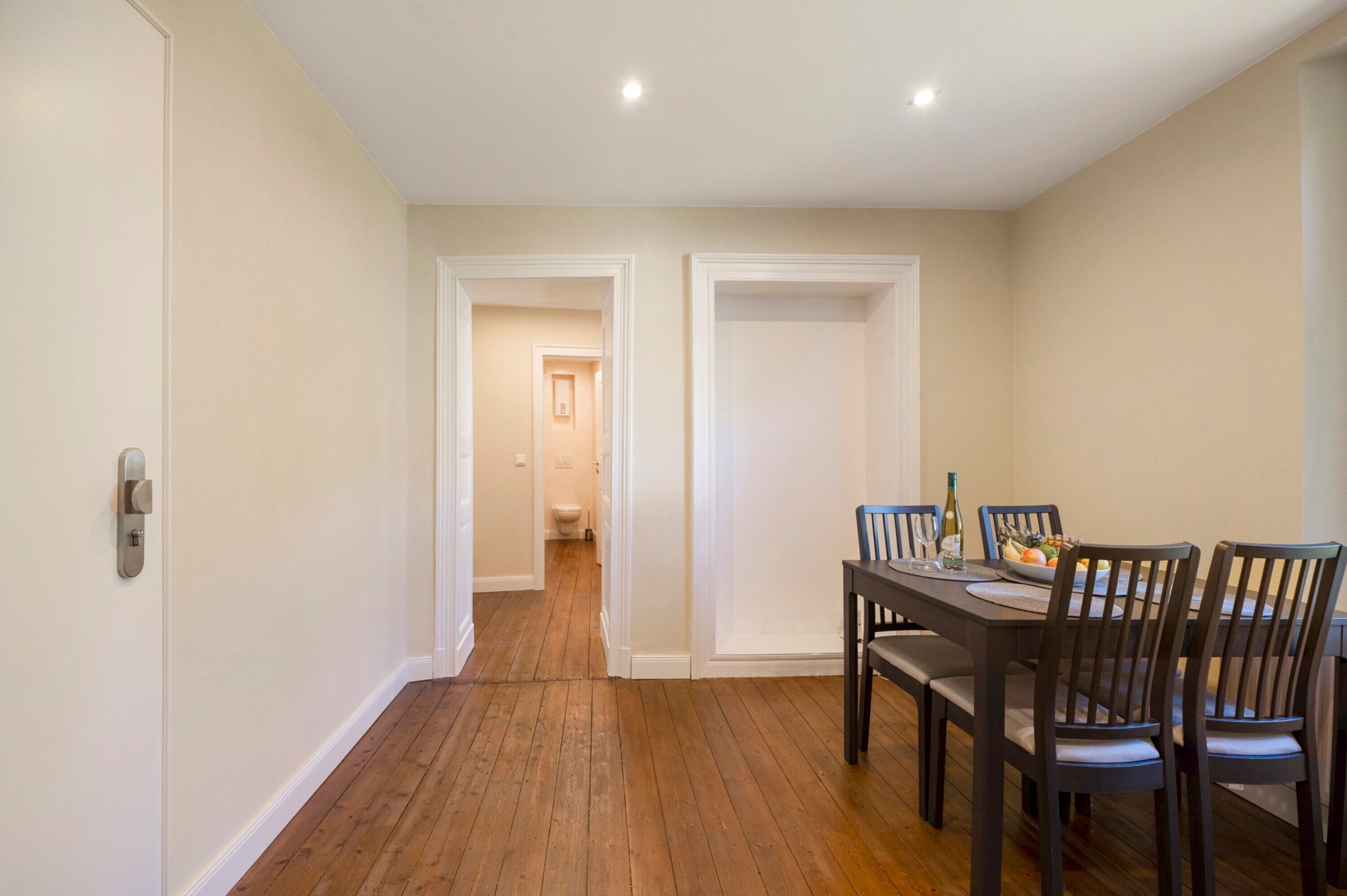 A dining area with a wooden floor, a dining table set for four, and a view into the adjacent bathroom.
