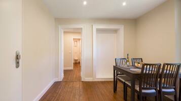 A dining area with a wooden floor, a dining table set for four, and a view into the adjacent bathroom.