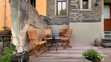 Un patio con sillas y una mesa de madera, una planta en maceta y un muro de piedra.