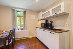 Una cocina con armarios blancos, encimera de madera, ventana con cortinas y una zona de comedor con mesa y sillas.