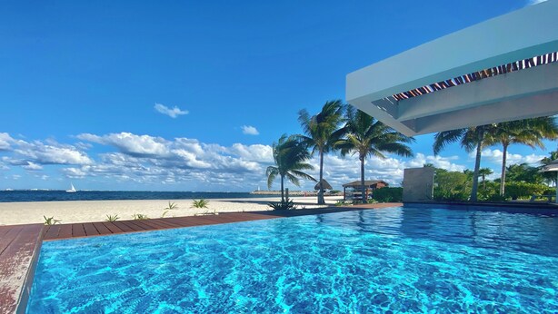Une piscine d’eau cristalline, avec une terrasse en bois, des palmiers et une vue sur la plage.