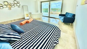 Une chambre moderne avec un grand lit, un canapé bleu, une baignoire et une grande fenêtre donnant sur l’extérieur.