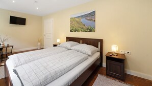 Um quarto com uma cama grande, mesas de cabeceira, uma televisão e um quadro de uma paisagem.