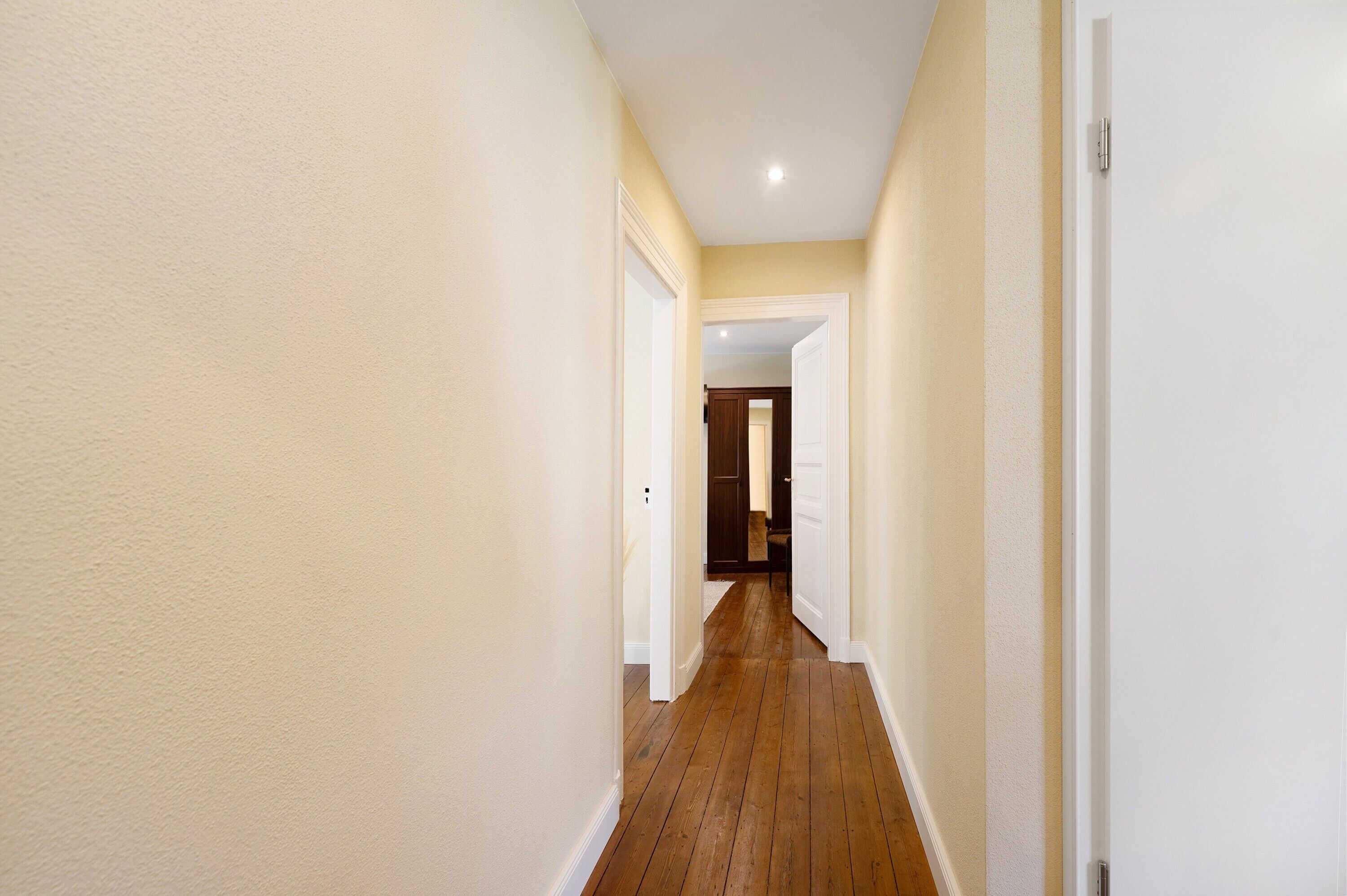 A narrow hallway with wooden flooring and white walls.