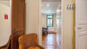 Um corredor com um guarda-roupa de madeira, uma poltrona acolchoada, uma área de refeições com mesa e cadeiras, e uma janela com vista.