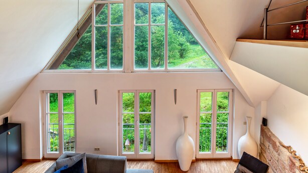 Una habitación con techo inclinado, ventanas amplias, chimenea y un sofá.