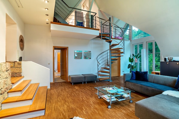 A spacious living area with a wooden staircase, a glass coffee table, and a modern staircase.