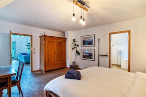 A bedroom with a bed, wooden wardrobe, and a dining area with a table and chairs.