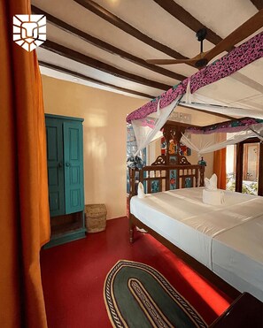 Un dormitorio con cama, cabecera de madera, mesita de noche, puerta azul y alfombra roja.