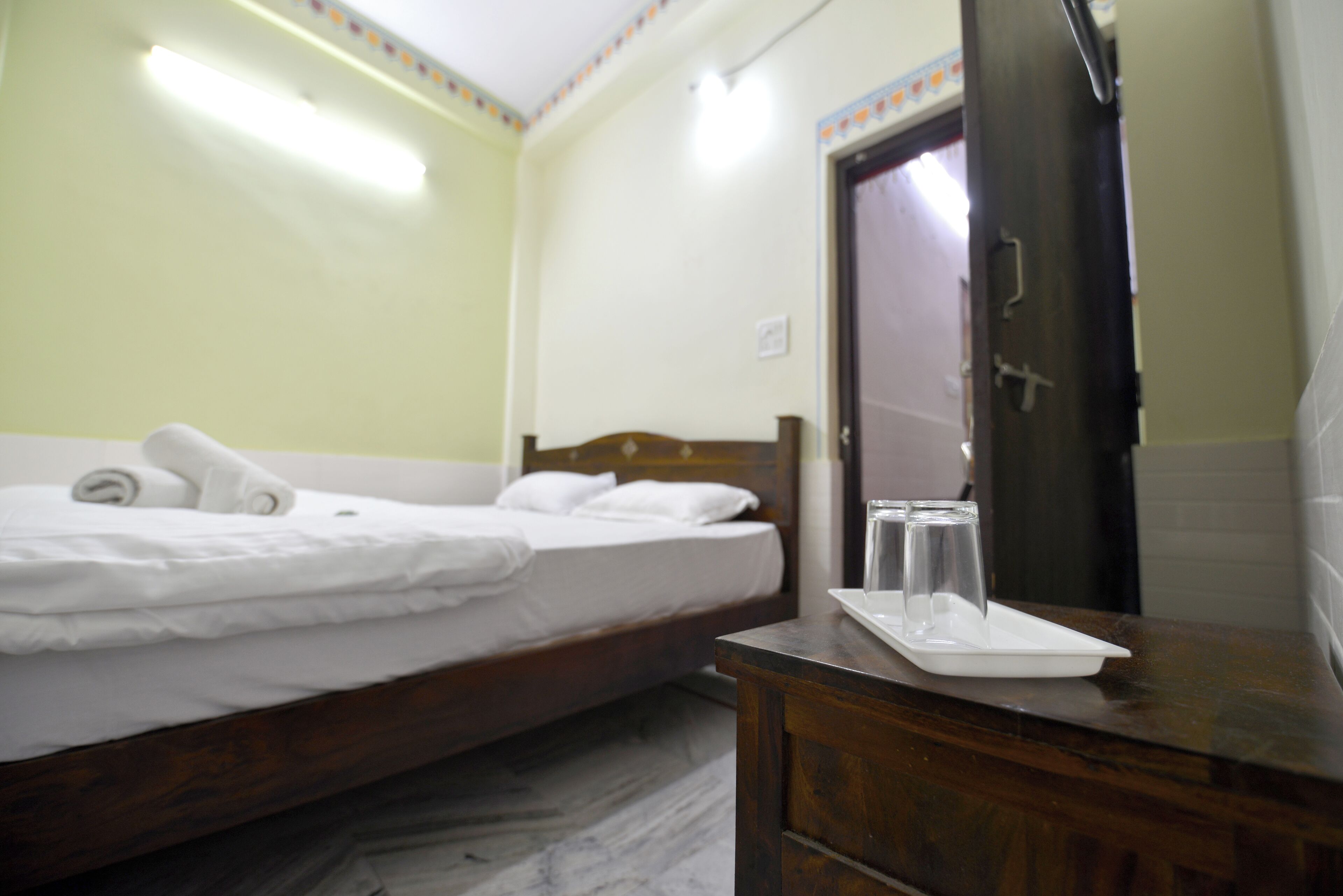 Habitación de hotel con cama, cómoda de madera, espejo y una mesita con un vaso y una bandeja.