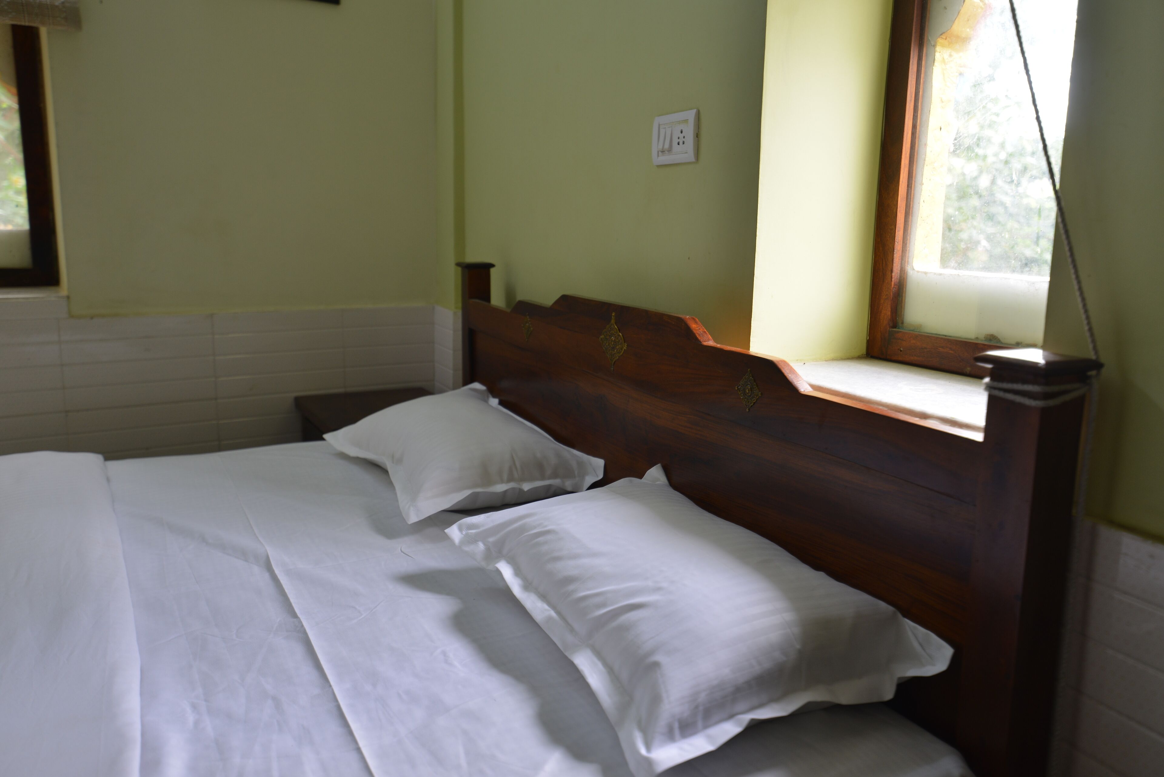 Un letto rifatto con lenzuola e cuscini bianchi in una stanza con una testiera in legno e una finestra che si affaccia sul verde.