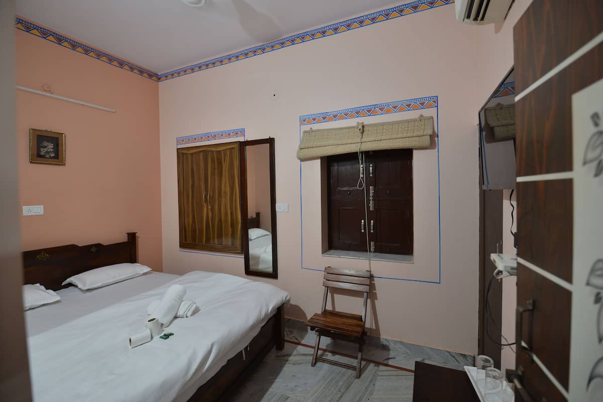 Una habitación de hotel con cama, una silla, un ventanal con cortina, un espejo y un armario.