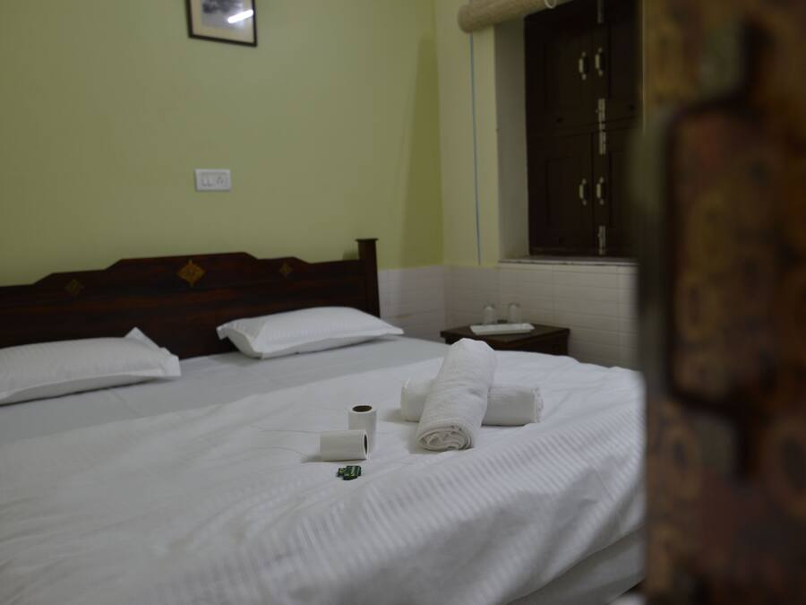 A hotel room with a bed, pillows, a small table with a cup and a tissue box, and a window with curtains.