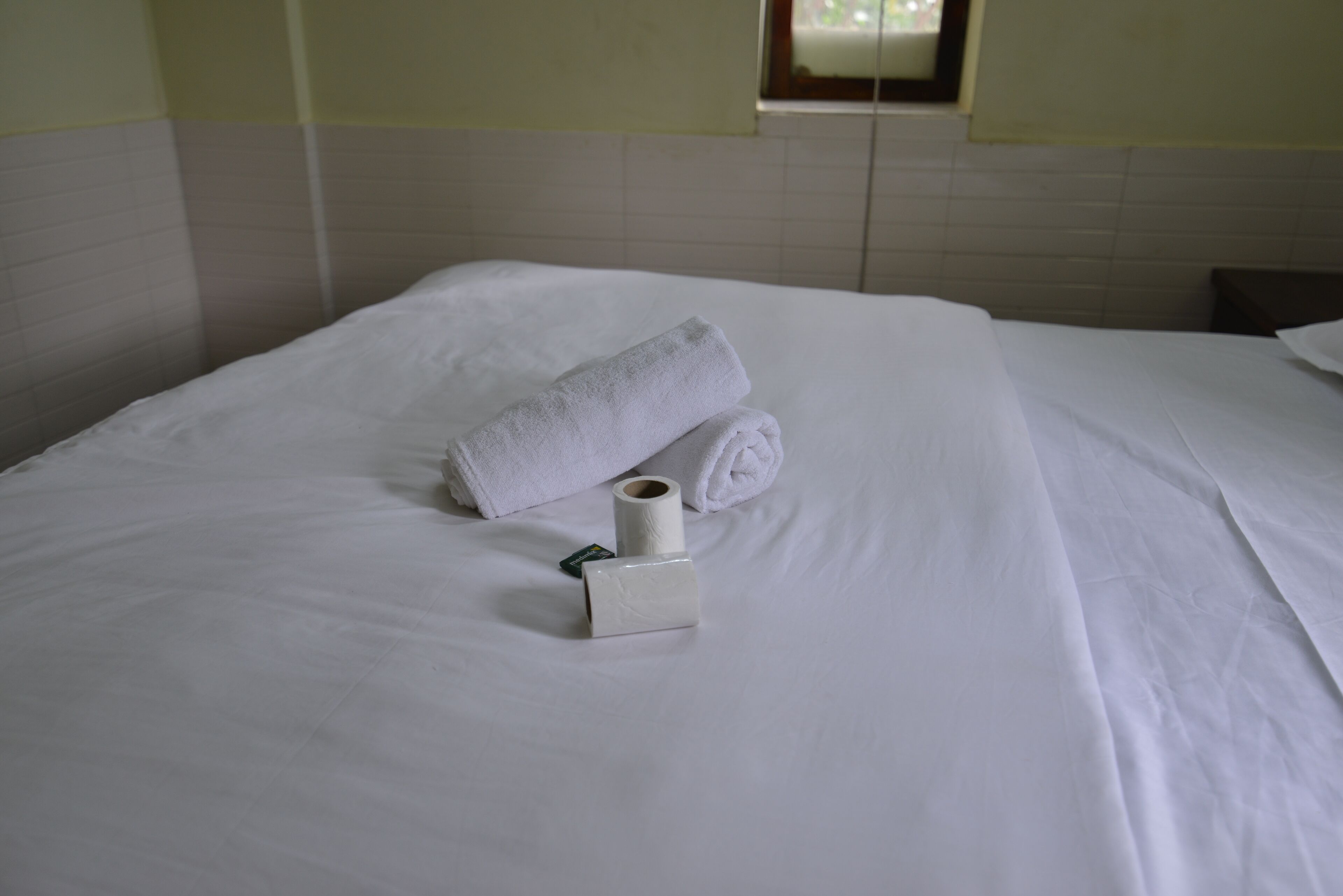 Cama bem arrumada com uma toalha enrolada e uma caixa de lenços.