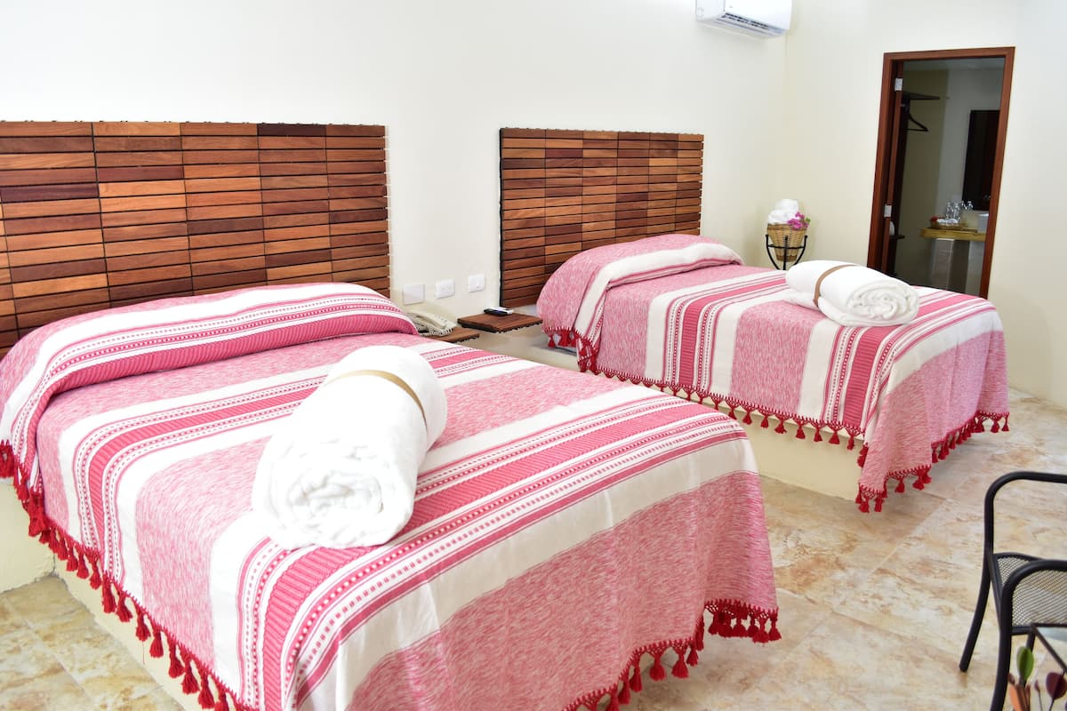 Une chambre d'hôtel avec deux lits, chacun recouvert d'une courtepointe à rayures roses et blanches, et une serviette blanche posée sur l'un des lits.