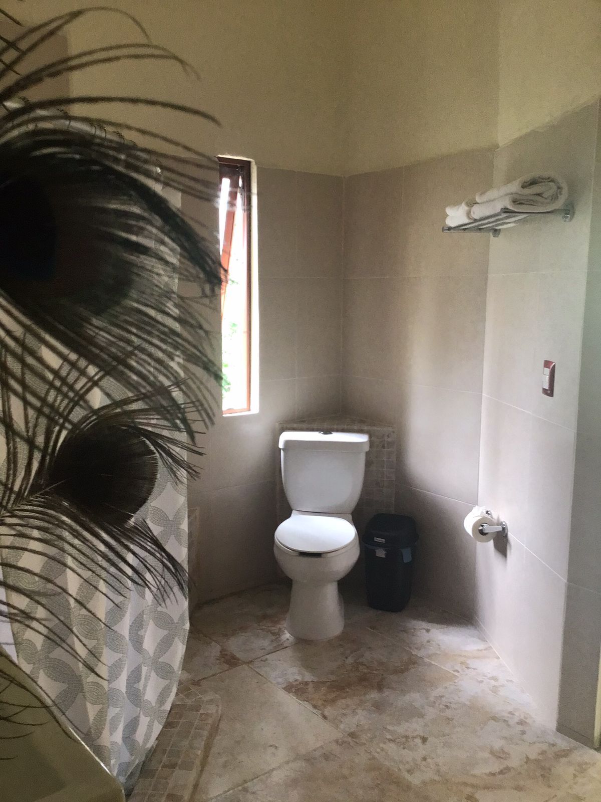 A small, tiled bathroom with a toilet, a trash bin, and a towel rack.