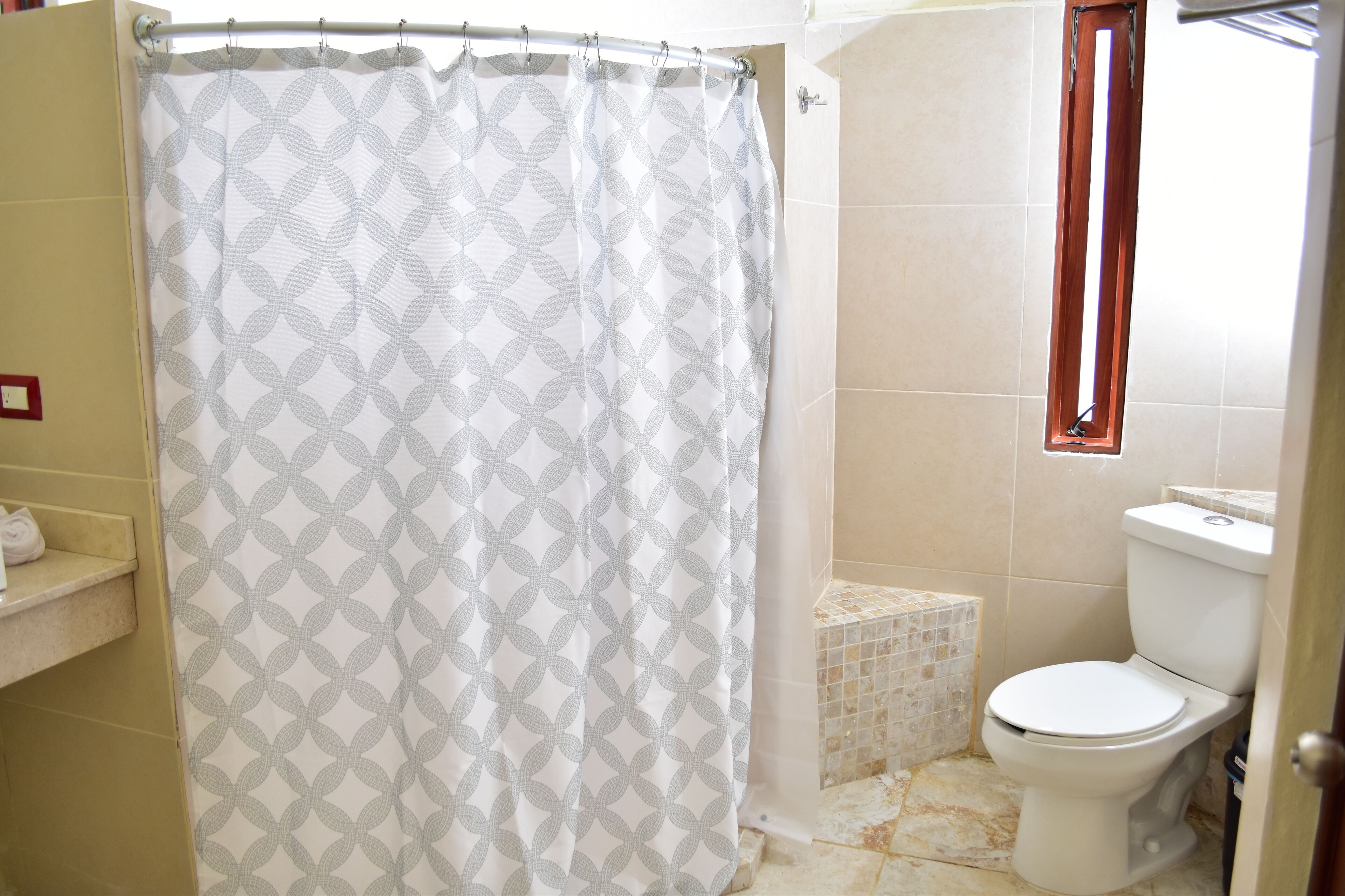 A bathroom with a shower curtain, a toilet, and a small tiled area.