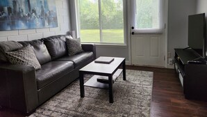 Ett vardagsrum med en mörk lädersoffa, ett soffbord, en tavla på väggen och en dörr med persienner.