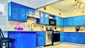 A modern kitchen with blue cabinets, stainless steel appliances, and a bar stool.