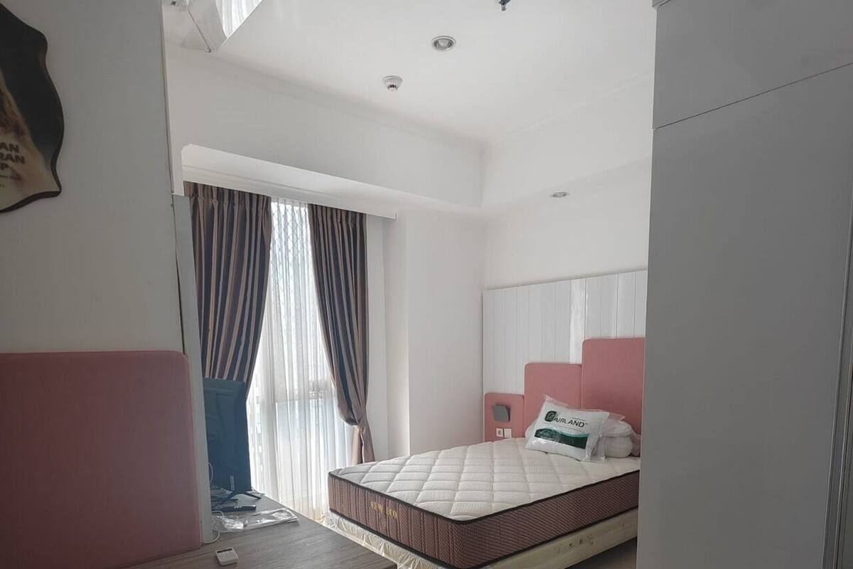 A bedroom with a bed, a desk, a wardrobe, and a window with curtains.