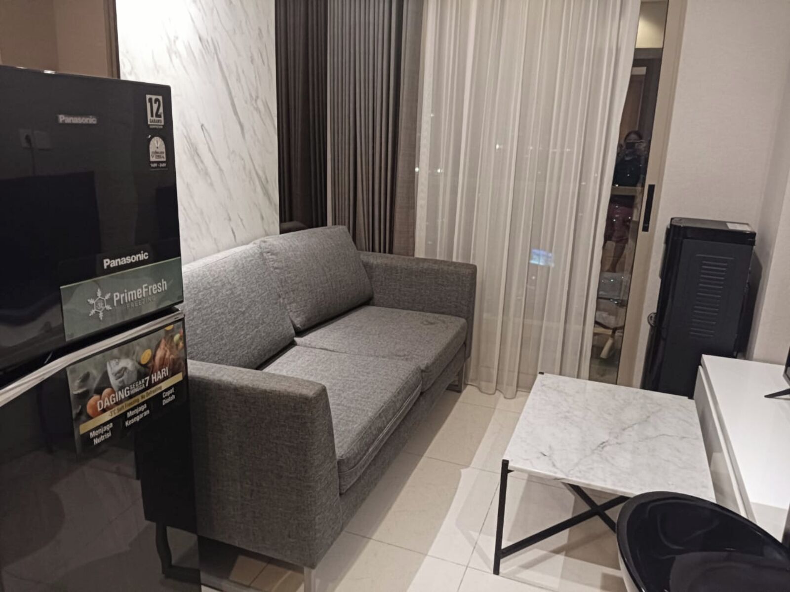 Habitación de hotel moderna con sofá gris, televisión de pantalla plana, piso de baldosas de mármol y una pequeña mesa.