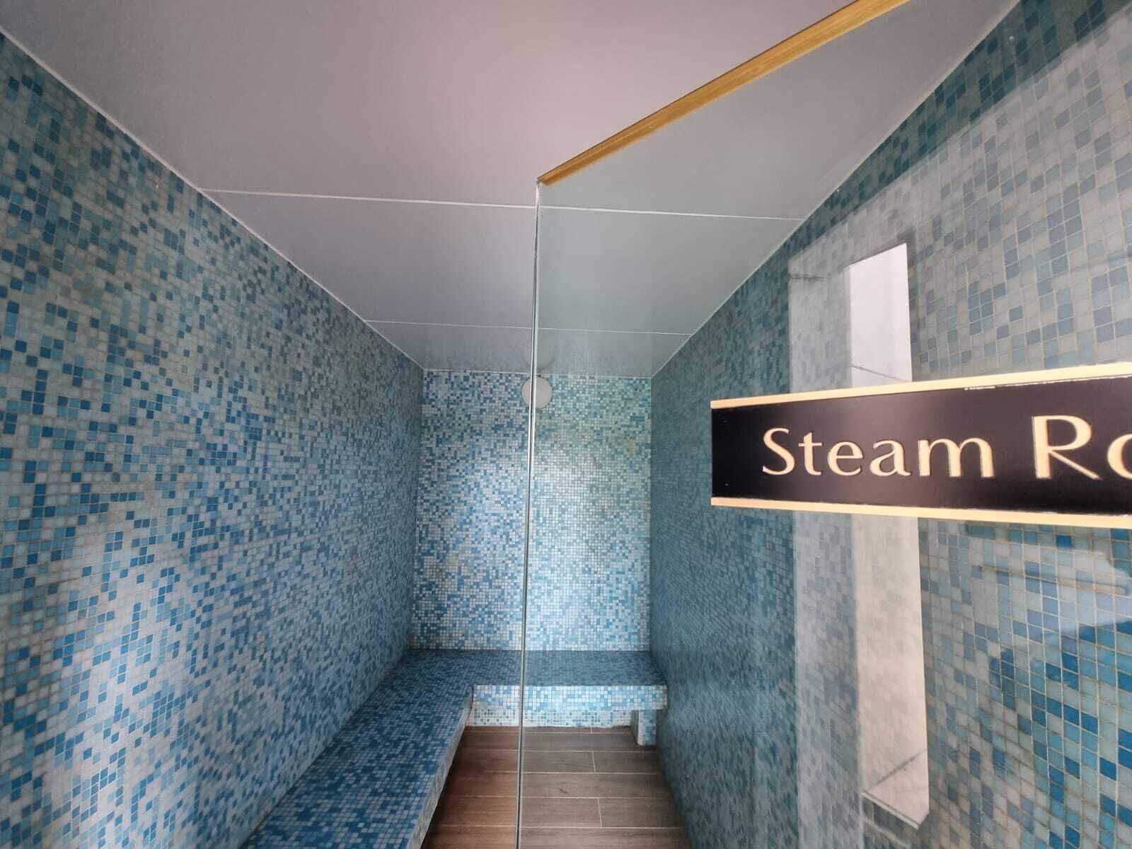 A modern bathroom with mosaic tile walls and a bench. A sign reads "Steam Room."