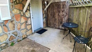 A stone house with a white door, a wooden fence, and a small patio with two metal chairs and a table. - D'vinery Rock Cottage/ #6 (Eureka Springs)