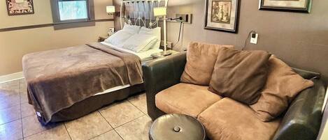 A hotel room with two beds, a sofa, a trash bin, and framed pictures on the walls.
