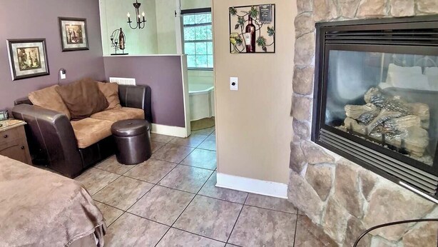 A living room with a stone fireplace, a sofa, a coffee table, and framed pictures on the wall. - D'vinery Rock Cottage/ #6 (Eureka Springs)