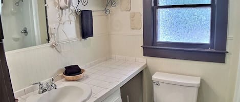A bathroom with a white sink, a toilet, a towel rack with folded towels, and a window with frosted glass.