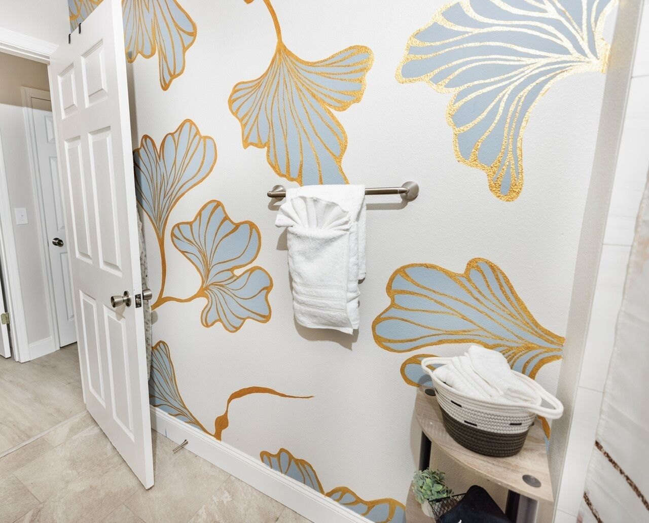 Une salle de bain avec un motif floral sur le mur, un porte-serviettes et un panier rempli de serviettes.