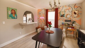 A dining area with a dark table, chairs, a vase with flowers, a chandelier, and a wall with abstract art and a shelf with items. - Downtown Orlando Creative Oasis- Hand Painted Murals & Free Parking.  (Orlando)