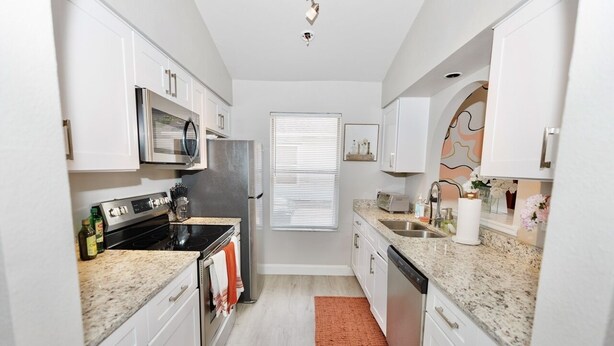A compact kitchen with white cabinets, a stainless steel refrigerator, a microwave, and a dishwasher. - Downtown Orlando Creative Oasis- Hand Painted Murals & Free Parking.  (Orlando)