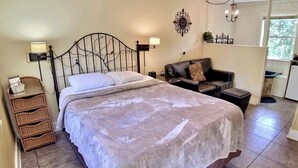 A bedroom with a bed, a nightstand, a dresser, a sofa, and a wall-mounted lamp. - Tuscany Dream Rock Cottage/#8 (Eureka Springs)