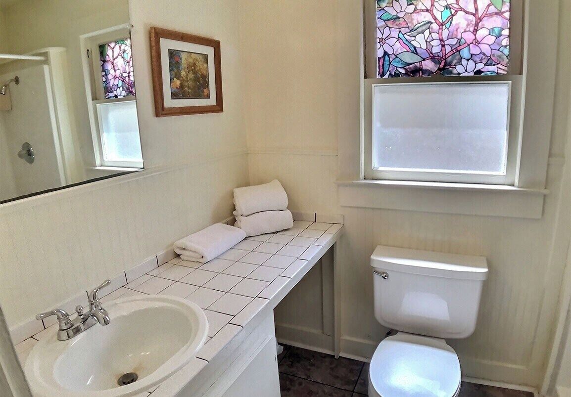 A bathroom with a white sink, toilet, and a window with stained glass.