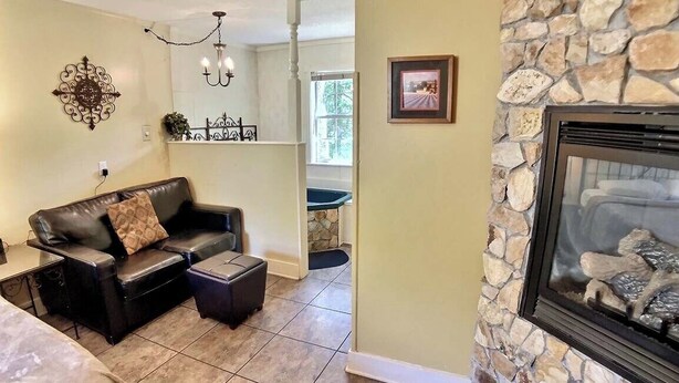A living room with a stone fireplace, a leather sofa, and a dining area visible through an open door. - Tuscany Dream Rock Cottage/#8 (Eureka Springs)