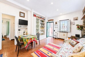 A living room with a sofa, a dining table with chairs, a television, and a bookshelf.