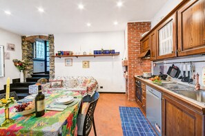 A kitchen with wooden cabinets, a brick wall, a dining area with a table set for two, and a staircase leading to an upper level.