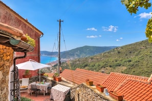 A terrace with a table and chairs, potted plants, and a view of the sea.