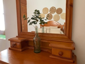 A wooden vanity with a mirror, a vase with green leaves, and a wooden headboard with a decorative headboard.