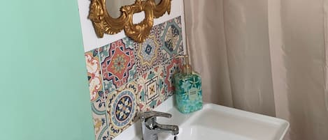 A bathroom with a white sink, a gold ornate mirror, and a colorful tile backsplash.