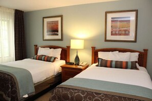 Habitación de hotel con dos camas, una mesita de noche con lámpara y cuadros en la pared.